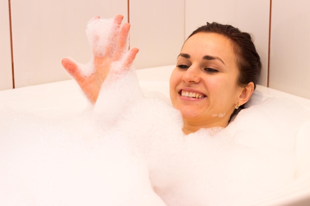 Young charming woman with bundle on her head lying in the bath full of foam