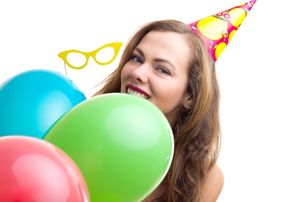 Young charming woman with long chestnut hair with celebrating hat holding many colored balloons