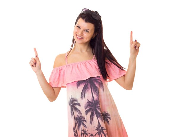 Young charming woman with long dark hair in pink dress with palm trees and black sunglasses dancing on white background in studio