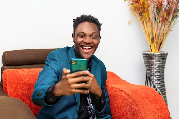 Young cheerful african american man sitting in chair holding mobile phone