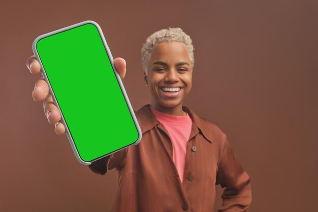 Young cheerful african american woman holds out hand with phone to camera