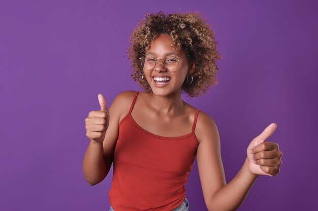 Young cheerful african american woman shows two thumbs up stands in studio