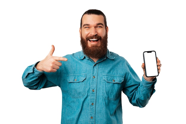 Young cheerful bearded man pointing at his phone screen with copy space