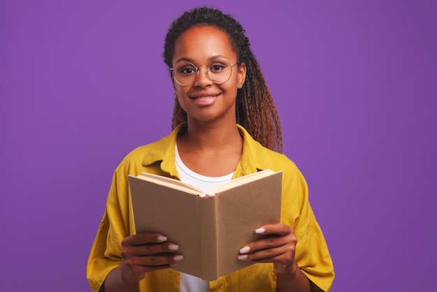 Young cheerful casual african american woman teacher with book stands in studio