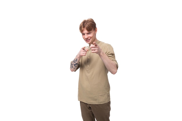 Young cheerful caucasian man with red hair is dressed in a khaki shirt and brown trousers