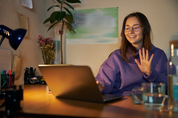 Young cheerful confident and happy freelancer woman is working on laptop at home in the evening