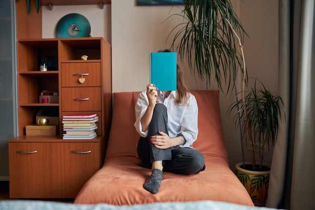 Photo young cheerful confident and happy woman is relaxing at her cozy armchair at home with books