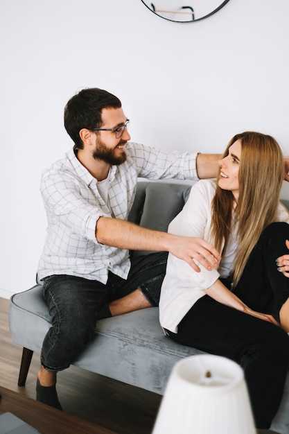 Young cheerful couple heaving fun on a sofa at home and hugging each other.