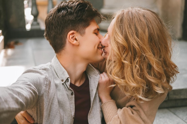 Young cheerful couple is taking a selfie while giving a kiss to each other