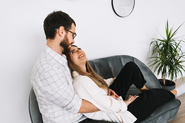 Photo young cheerful couple resting on a sofa at home, gently touching each other.