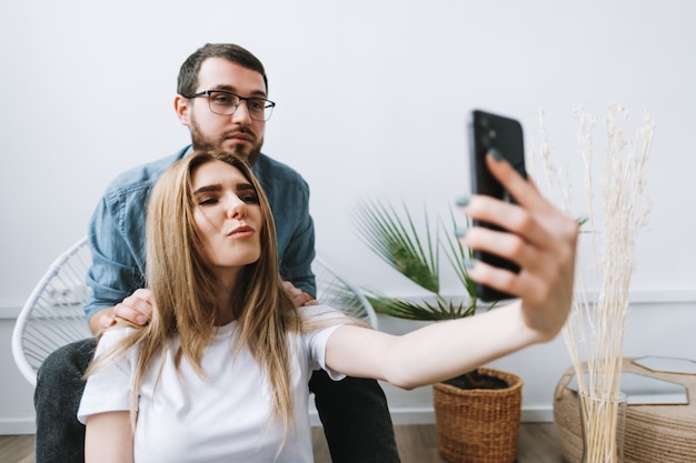 Young cheerful couple using mobile phone, making selfie on smartphone together.