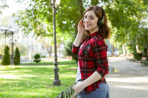 若い陽気なおかしい女性は、都市公園でヘッドフォンで音楽を聴きます