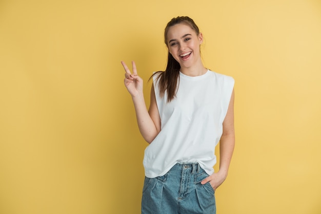 Young cheerful girl happy positive smile show peace cool vsign isolated over yellow color background