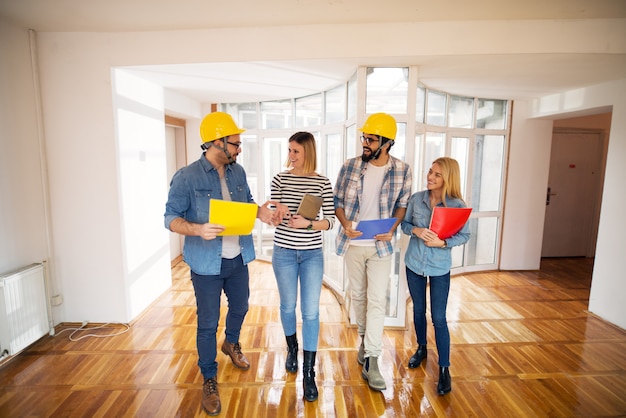 Young cheerful group of male engineers and female designers walking down the hallway while talking and laughing.