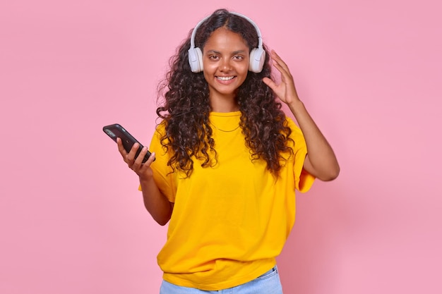 Young cheerful indian woman listens to music on headphones and holds phone