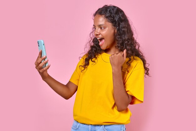 Young cheerful indian woman teen screams and looks at screen of mobile phone