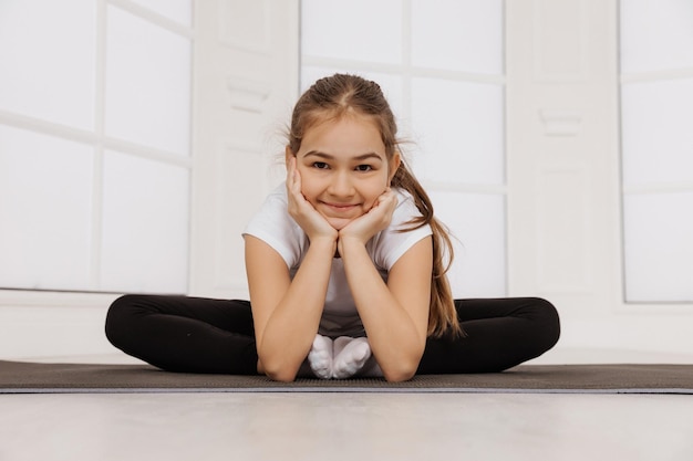 Фото Молодая веселая девочка делает упражнения на коврике для фитнеса, смотрит в камеру и улыбается
