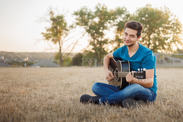 Молодой жизнерадостный человек играя гитару снаружи. Позитивный настрой музыканта.