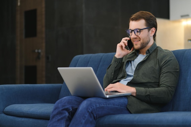 Young cheerful man sitting on sofa with laptop