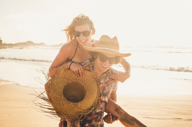 I giovani allegri che si divertono in coppia con l'uomo portano una bella donna - ridendo insieme e godendosi la giornata di sole delle vacanze in spiaggia - concetto di romanticismo e amore