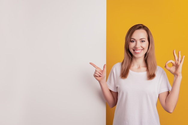 Foto la giovane donna positiva allegra che indica il bordo bianco dello spazio vuoto mostra il segno giusto?