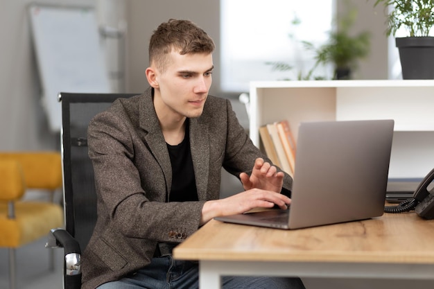 Young cheerful programmer working in office on laptop