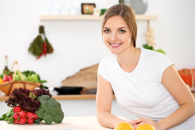 Young cheerful smiling woman is ready for cooking in a kitchen Housewife sitting at the table and looking at the camera