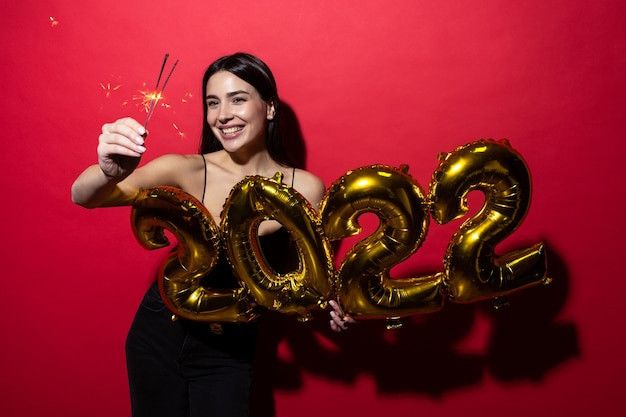 A young cheerful woman in a black dress holds the numbers 2022 and sparklers.