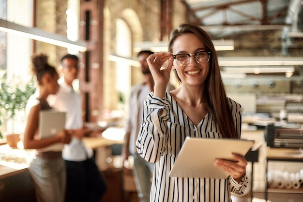 young cheerful woman holding digital tablet with smile while standing in the office