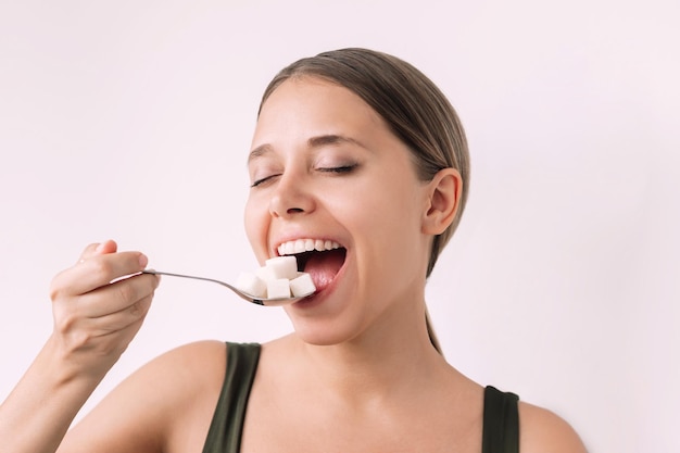 Young cheerful woman holding a spoon with cubes of refined sugar near her mouth