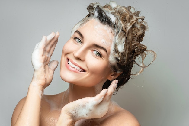 Young cheerful woman is washing her hair with a shampoo