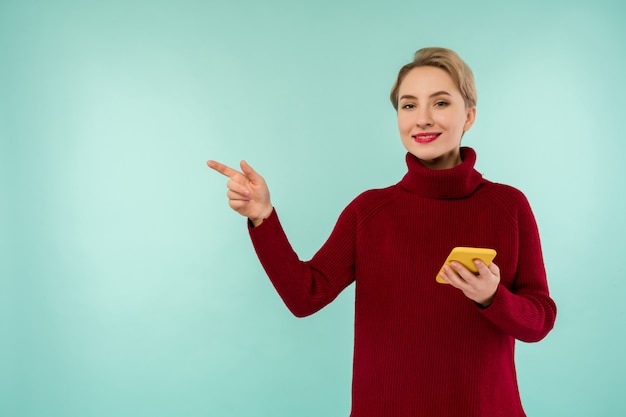 A young cheerful woman in a red sweater with a smartphone on a blue background
