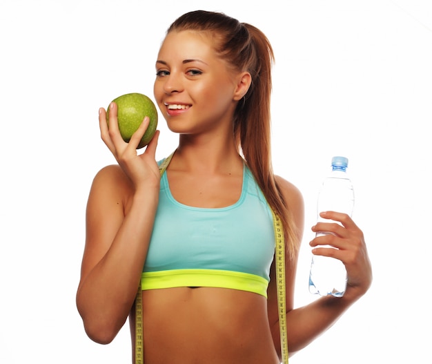 Young cheerful woman in sports wear with apple and water, isolated over white