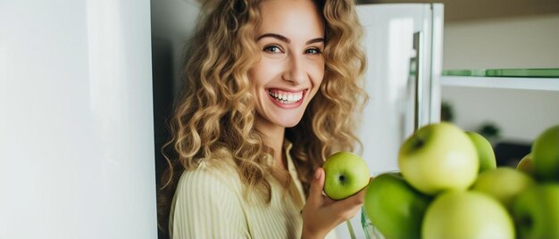 Photo young cheerful woman taking a green apple from refrigerator and smiling at camera