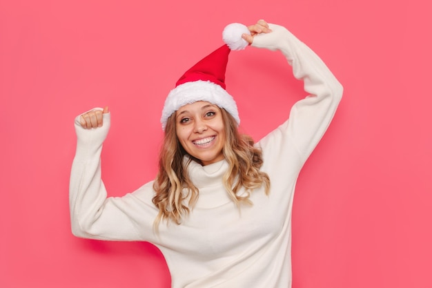 A young cheerful woman in a white sweater Christmas Santa hat is happy with her hands up