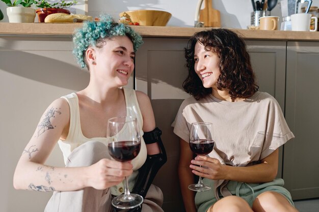 Photo young cheerful woman with disability and her girlfriend toasting with red wine