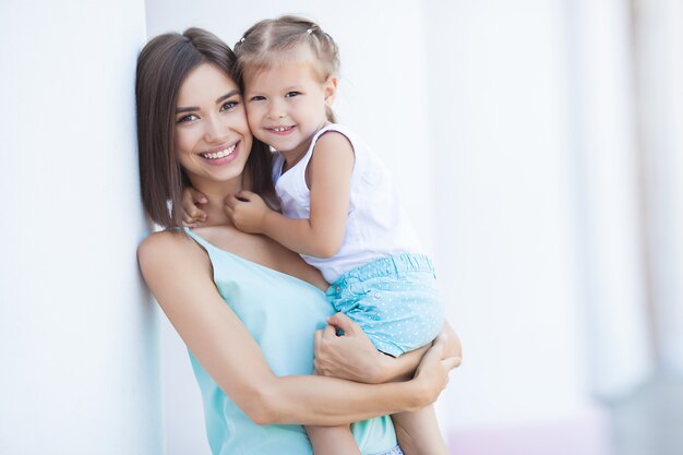 Young cheerful woman with her little daughter outdoors. Happy family together in summertime. Mom and child hugging.