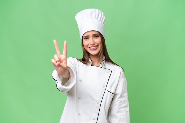 Young chef caucasian woman over isolated background smiling and showing victory sign