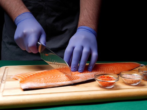 A young chef cuts a fresh raw salmon fillet and spices lie nearby on a wooden cutting board. Healthy food concept