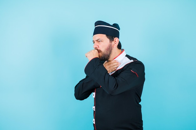Young chef is coughing by holding hand on mouth on blue background