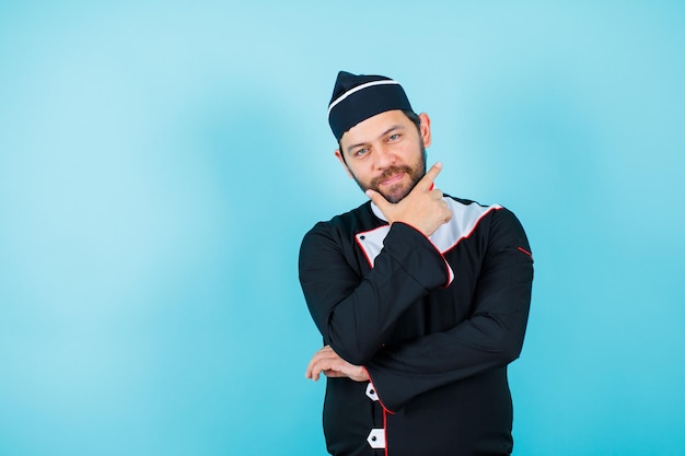 Il giovane chef sta guardando la fotocamera mettendo la mano sul mento su sfondo blu