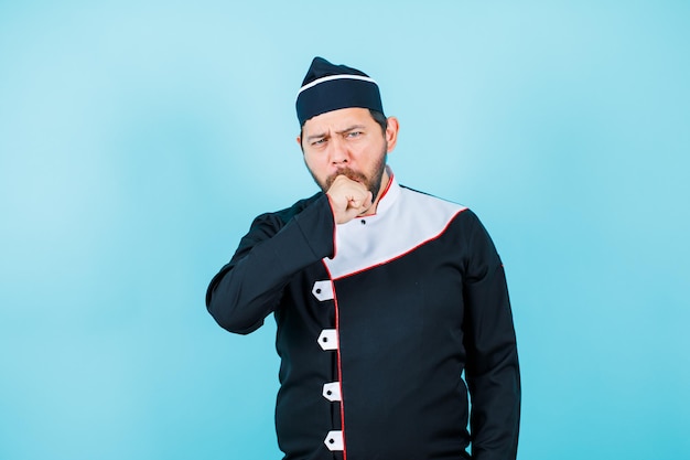 Young chef is yawing by putting hand on mouth on blue background