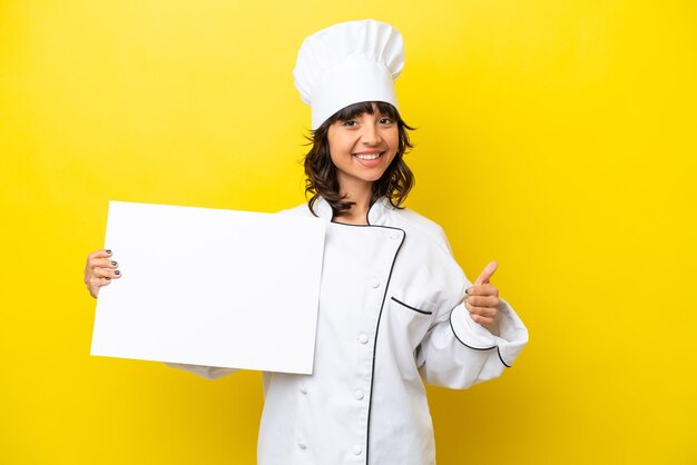 Young chef latin woman isolated on yellow background holding an empty placard with thumb up