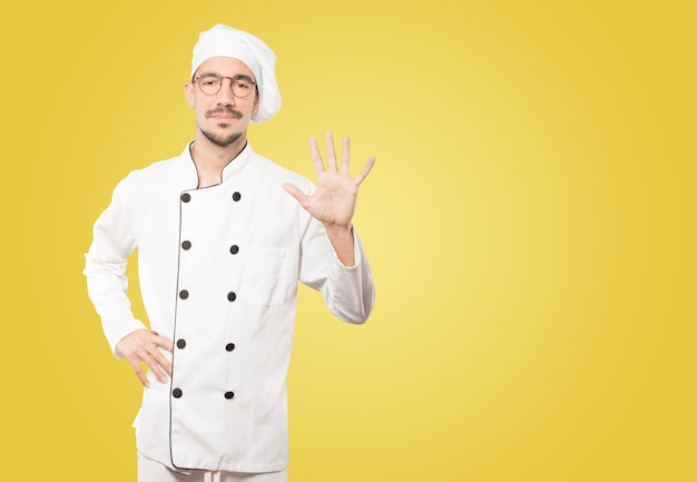 Young chef making a number five gesture