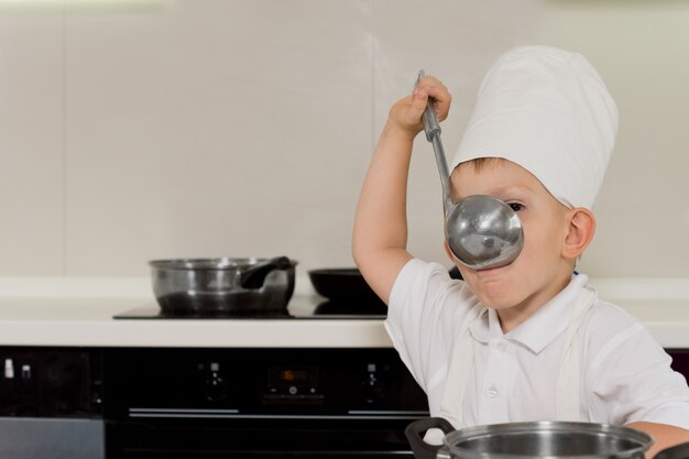 Young chef tasting soup from ladle in the kitchen