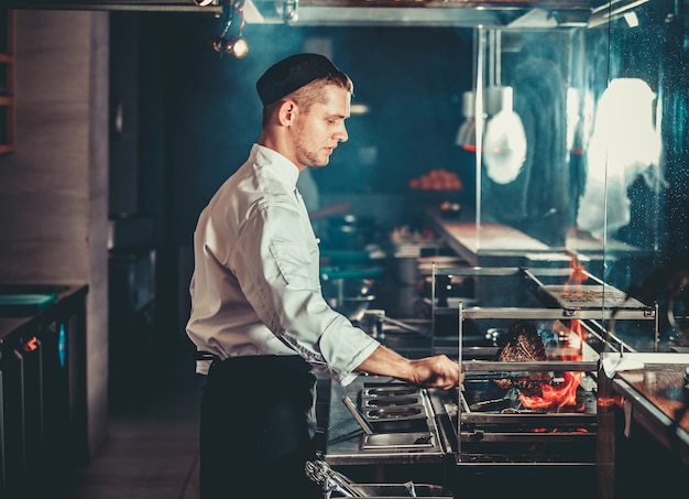 Young chef in white uniform cooking meat