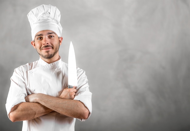 Young chef with knife posing with gray wall copyspace