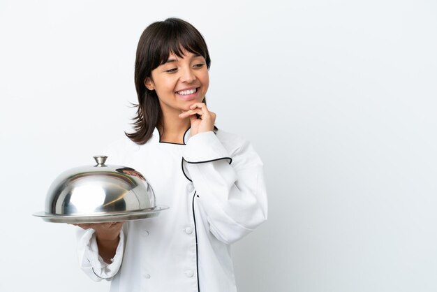 Young chef with tray isolated on white background looking to the side and smiling