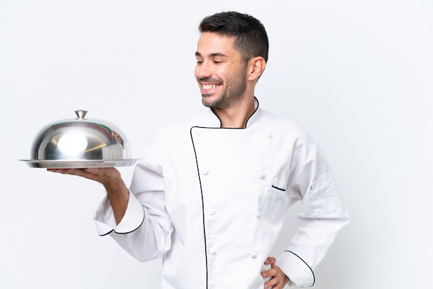 Молодой шеф-повар с подносом на белом фоне смотрит в сторону