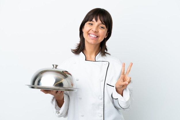 Young chef with tray isolated on white background smiling and showing victory sign